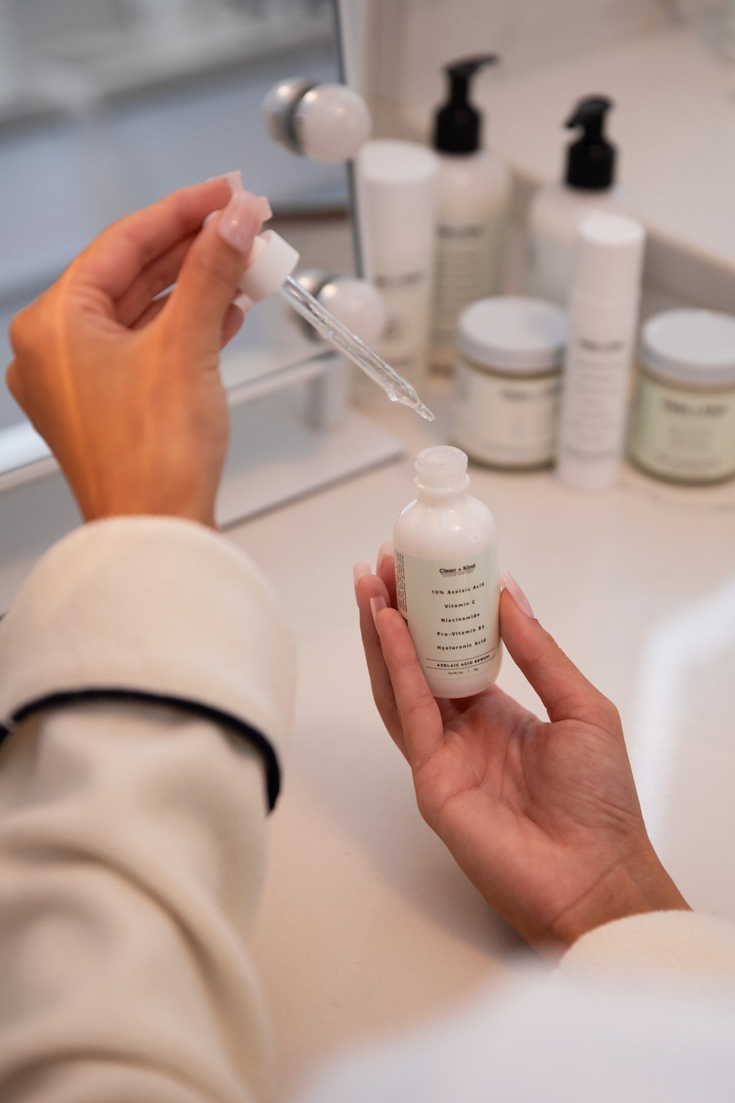 Person holding a dropper bottle with skincare products in the background